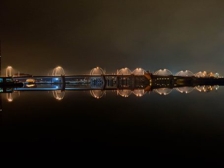 Landschap met waterreflectie van verlichte gebouwen en lantaarnpalen in de nacht.
