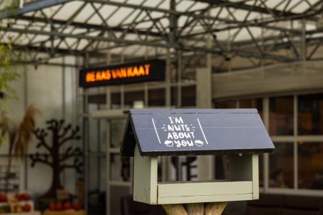 Een vogelhuisje met een bordje en een café op de achtergrond.