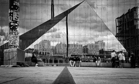 Abstracte spiegeling van een stad met pyramidevormige structuren en mensen in zwart-wit.