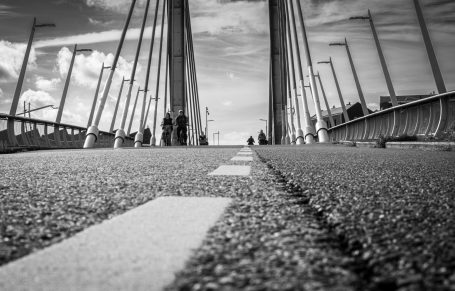 Zwart-witte afbeelding van een brug met mensen in de verte en een wegmarkering.