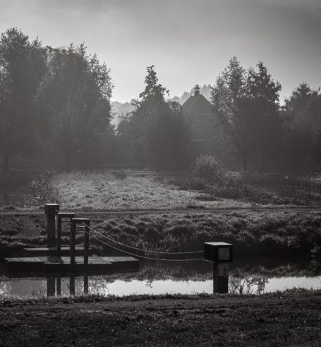 Zwart-wit landschap met een stille rivier, bomen en een mistige achtergrond.