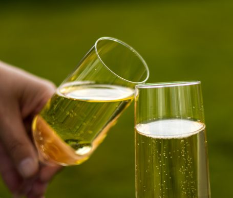 Twee glazen champagne klinken tegen elkaar op een groene achtergrond.