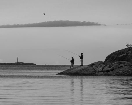 Twee mensen vissen vanaf een rotsachtige oever met een mistige achtergrond.